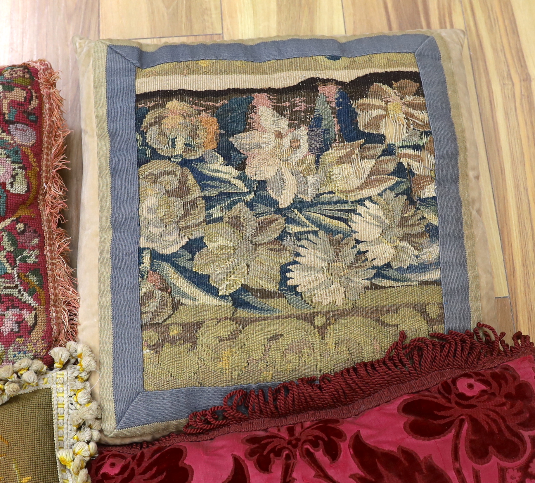 A late 18th century Flemish verdure tapestry fragment made into a cushion, a similar burgundy silk velvet damask cushion and two 19th early 20th century wool worked cushions (4)